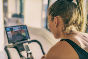 Pedal into the Peloton World 1 Smart Fitness Home Workout Biking Screen With Online Classes Woman Training On Stationary Bike Equipment Indoors For Biking Exercise. Indoor Cycling. Focus On The Sweat On Person's Back.