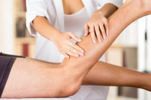 Closeup Female Physio Therapist Hands Working On Male Patients Legs, Blurry Clinic Background