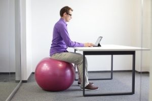 man on stability ball working with tablet - correct sitting position at workstation