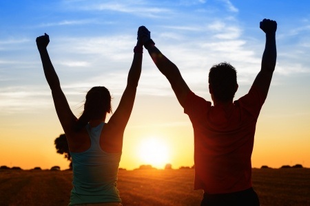 successful couple of young athletes raising arms