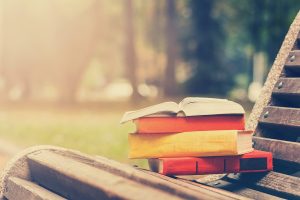 Stack of hardback books and Open book lying on bench