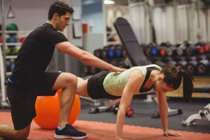 Fit Woman Working Out With Trainer At The Gym