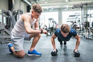 Young Fit Men In Gym Doing Push Ups On Dumbbells, Measuring Time On Smartwatch.